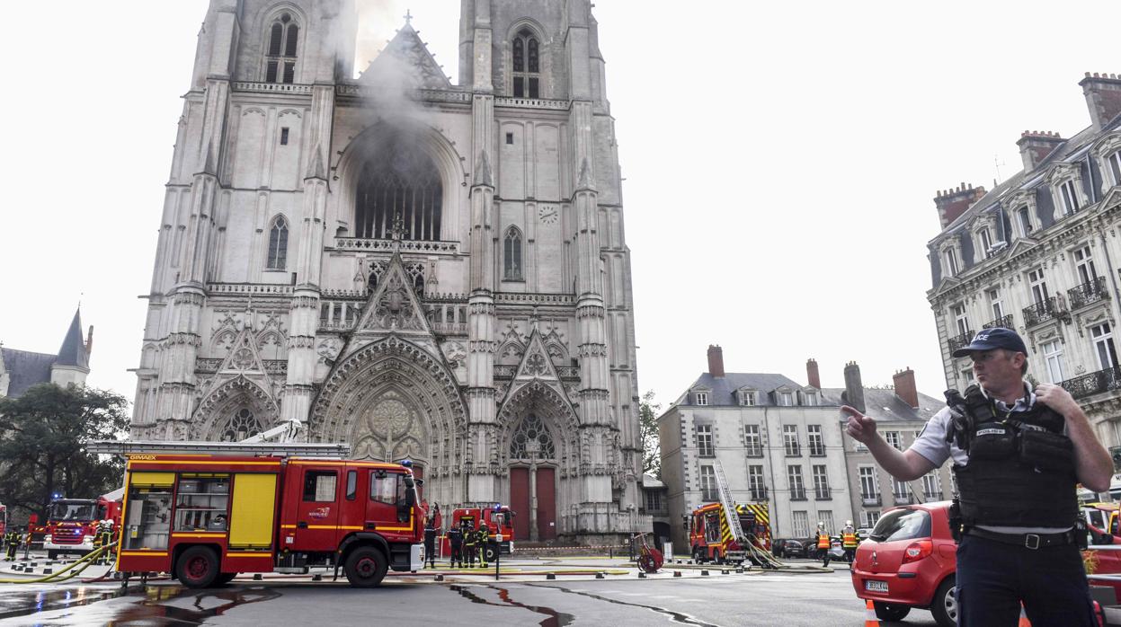 Un oficial de policía francés hace un gesto mientras los bomberos están trabajando para apagar un incendio en la catedral de Saint-Pierre-et-Saint-Paul en Nantes