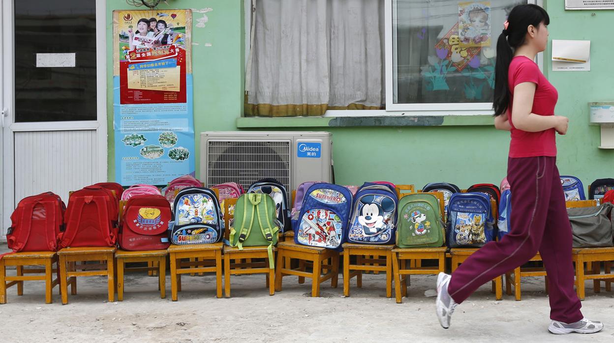 Una mujer pasa junto a mochilas escolares colocadas en sillas en un jardín de infancia en un pueblo en las afueras de Pekín