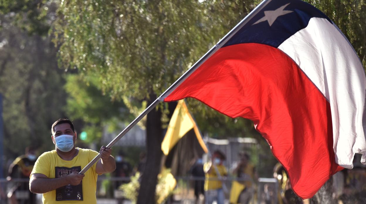 Un hombre, protegido con una mascarilla, sostiene una bandera de Chile
