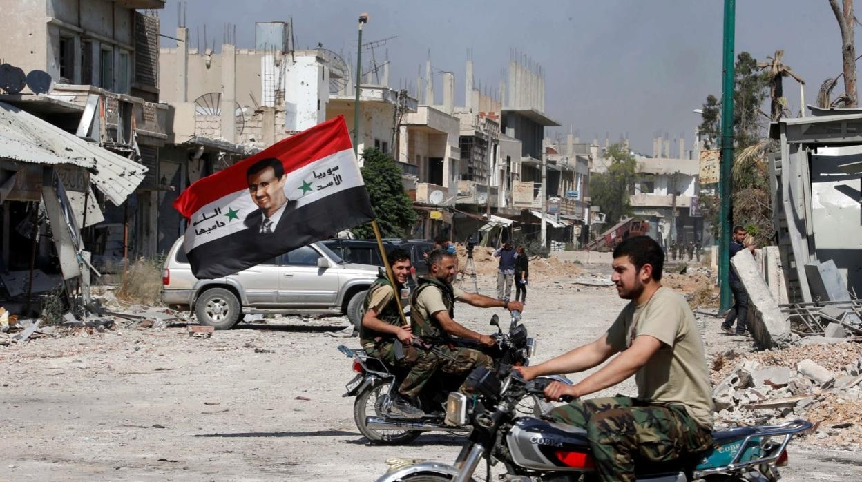 Fuerzas leales a Bashar al Assad sostienen la bandera de Siria con la cara del presidente