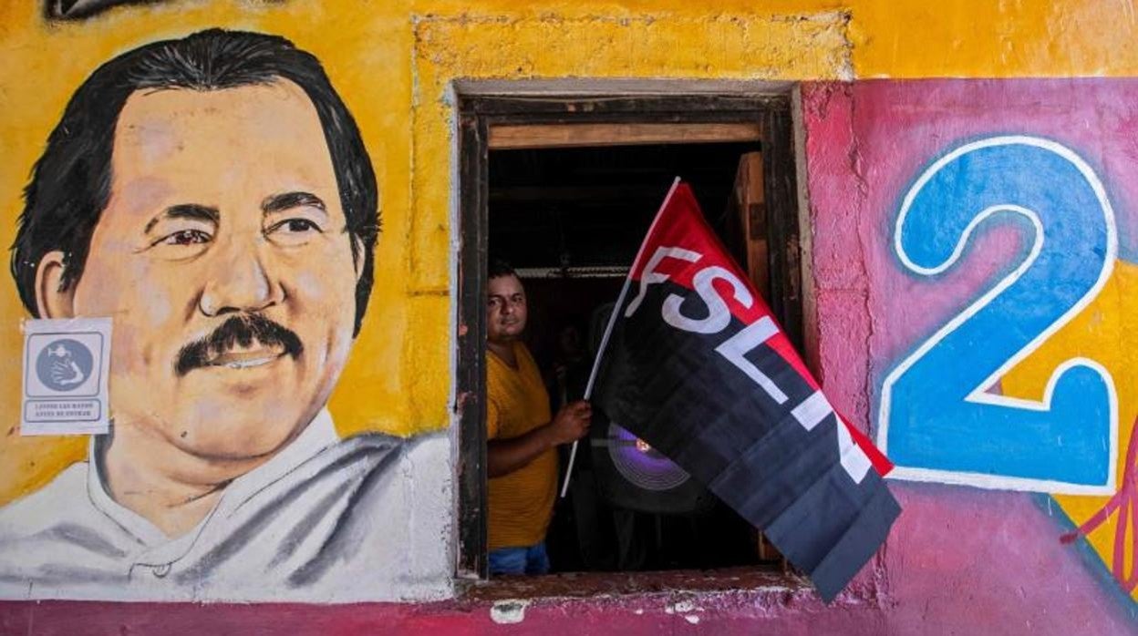 Un hombre sostiene una bandera del Frente Sandinista de Liberación Nacional (FSLN) junto a un retrato mural de Daniel Ortega en la sede del partido en Catarina