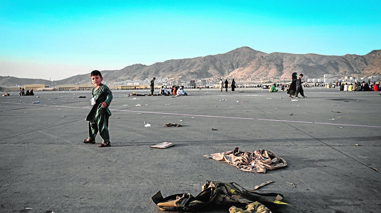 Un niño afgano camina solo cerca de varios uniformes militares en el aeropuerto de Kabul