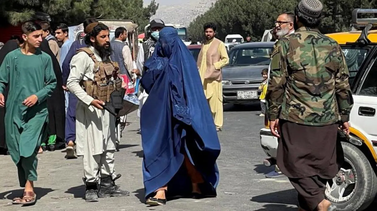 Fuerzas talibanes bloquean las carreteras de acceso al aeropuerto de Kabul, mientras pasa una mujer en burka