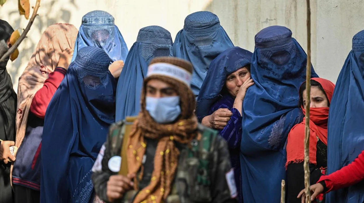 Un talibán controla fila de mujeres esperando en una cola recibir comida de un programa de ayuda, en Kabul