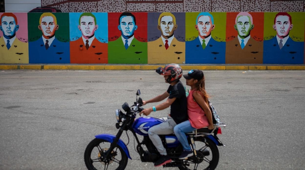 Una pareja pasa frente a un mural con la imagen del expresidente Hugo Chávez, en Barinas