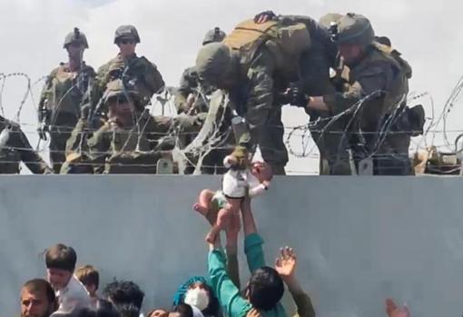 Militares de EE.UU. recogen a un bebé a través de un muro del perímetro del aeropuerto