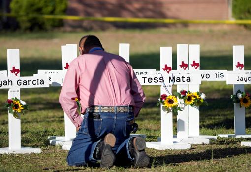 Un hombre reza ante cruces con el nombre de las víctimas