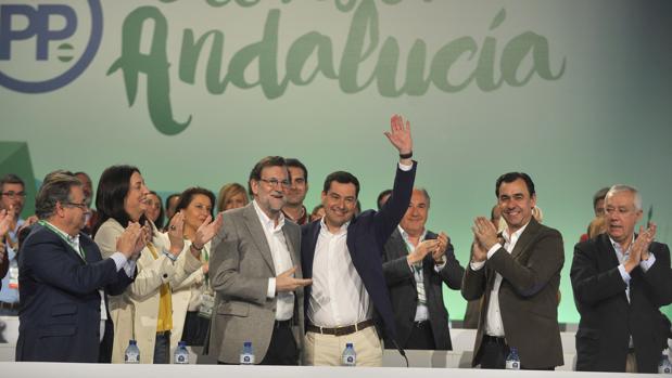 Juanma Moreno saluda al auditorio del congreso popular flanqueado por Mariano Rajoy y Martínez Maíllo