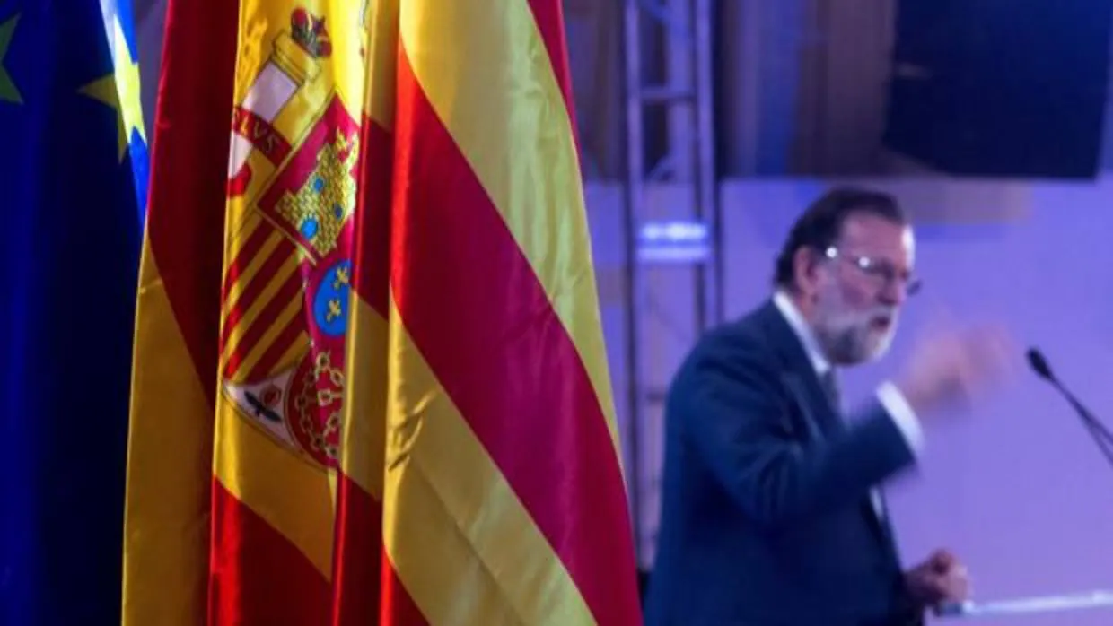 El presidente del Gobierno, Mariano Rajoy, junto a las banderas de la Unión Europea, de España y de Cataluña