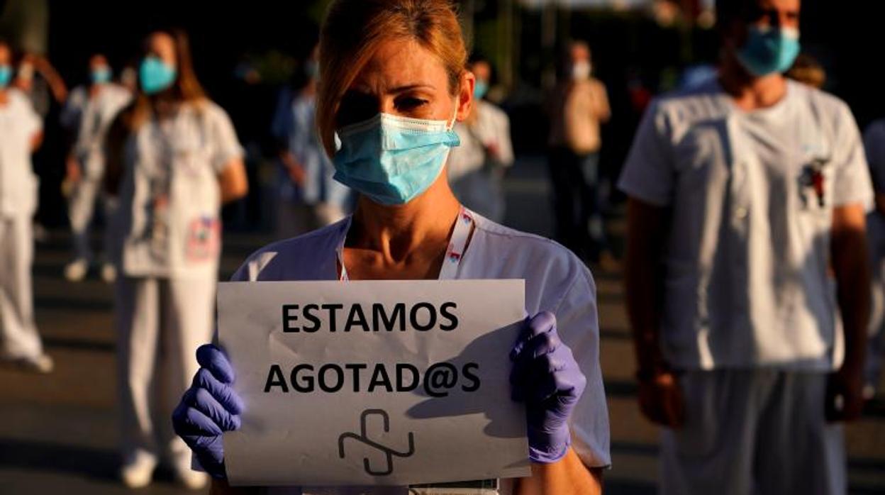 Una empleada del hospital de La Paz sostiene un cartel que dice «Estamos agotados» mientras asiste a una protesta para pedir más personal de salud en hospitales, atención primaria y asilos