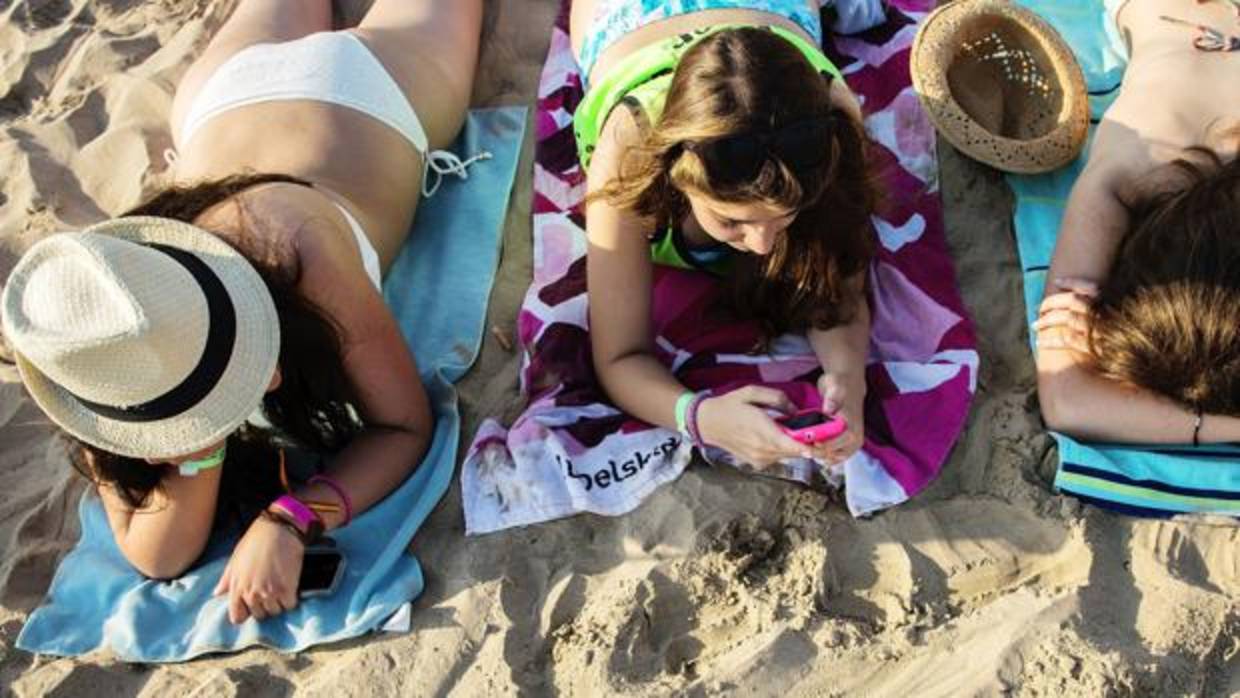 Dos jóvenes consultan sus teléfonos mientras están en la playa .