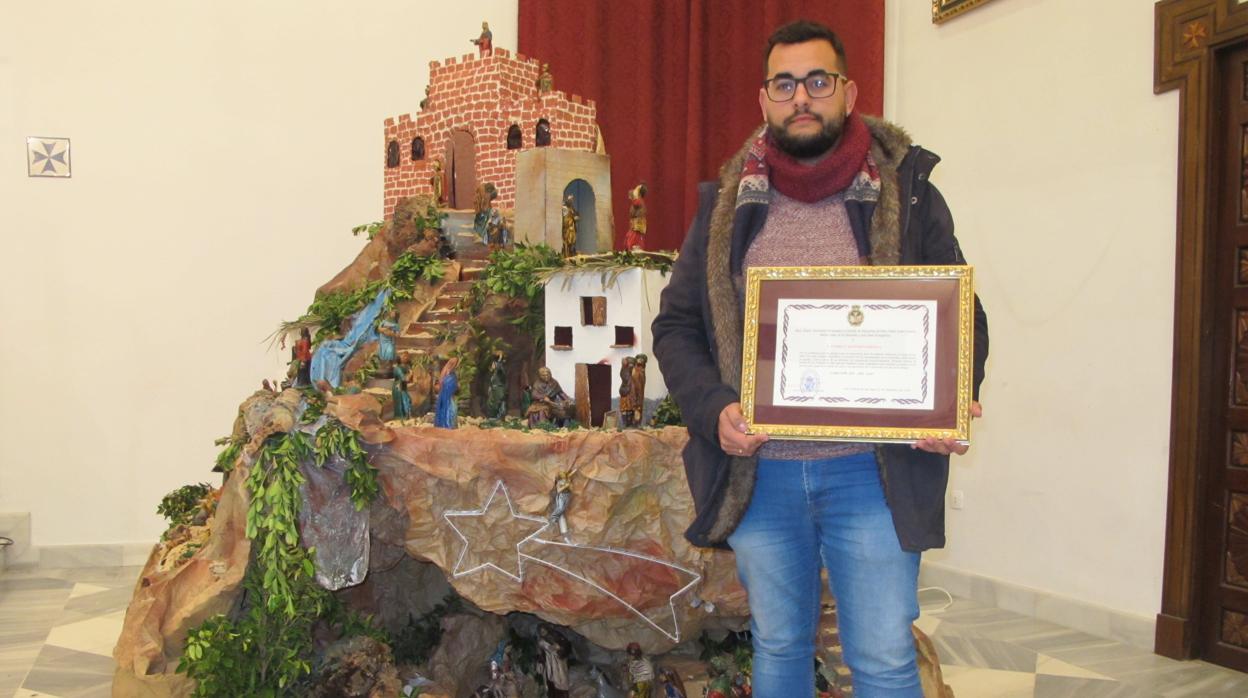 Enrique Maestre muestra el título de «Cabeceño del Año 2018» junto al belén de la capilla del Cautivo