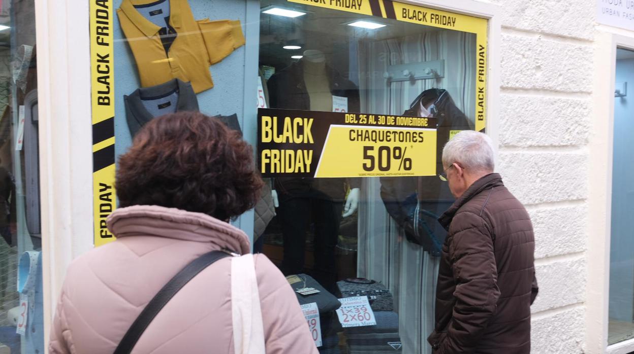 Varios clientes miran un escaparate con ofertas de Black Friday en Cádiz centro.