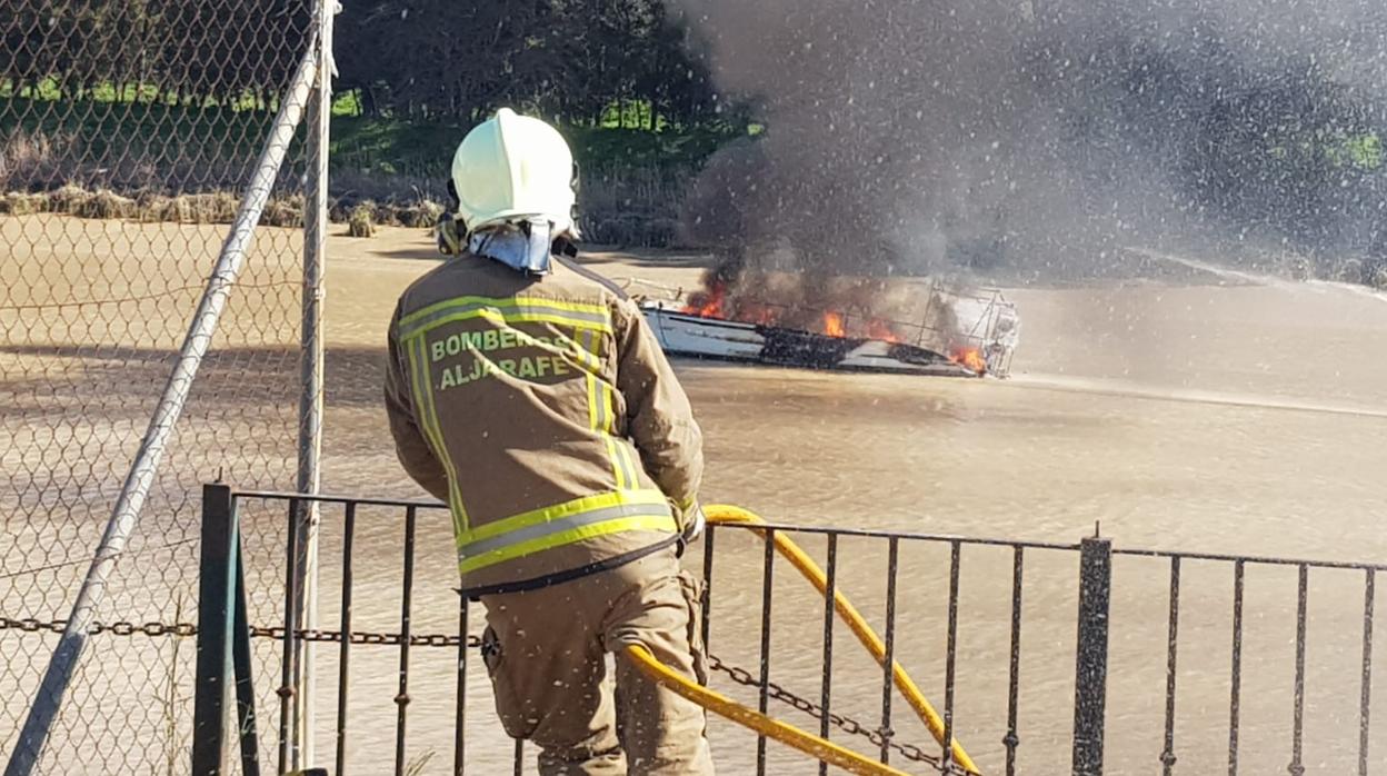 Un bombero sostiene una maguera ante el incendio de una embarcación en Gelves