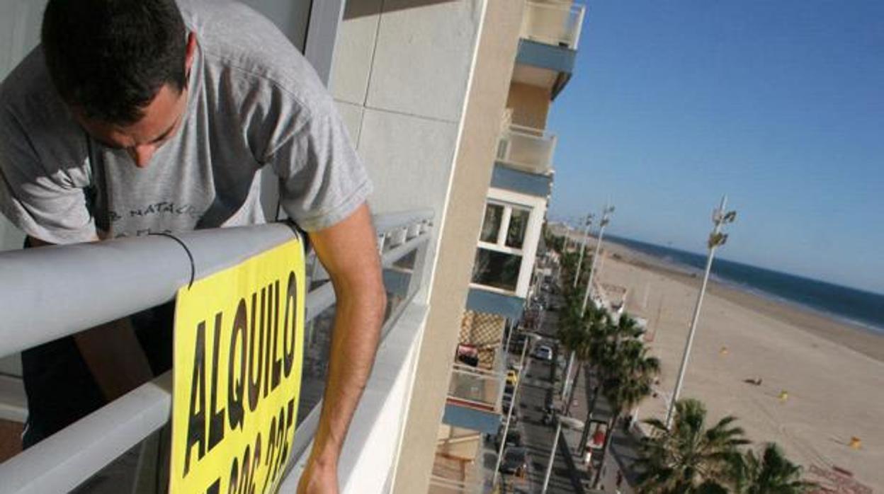 Un hombre pone el cartel de alquiler en una vivienda del Paseo Marítimo de Cádiz.