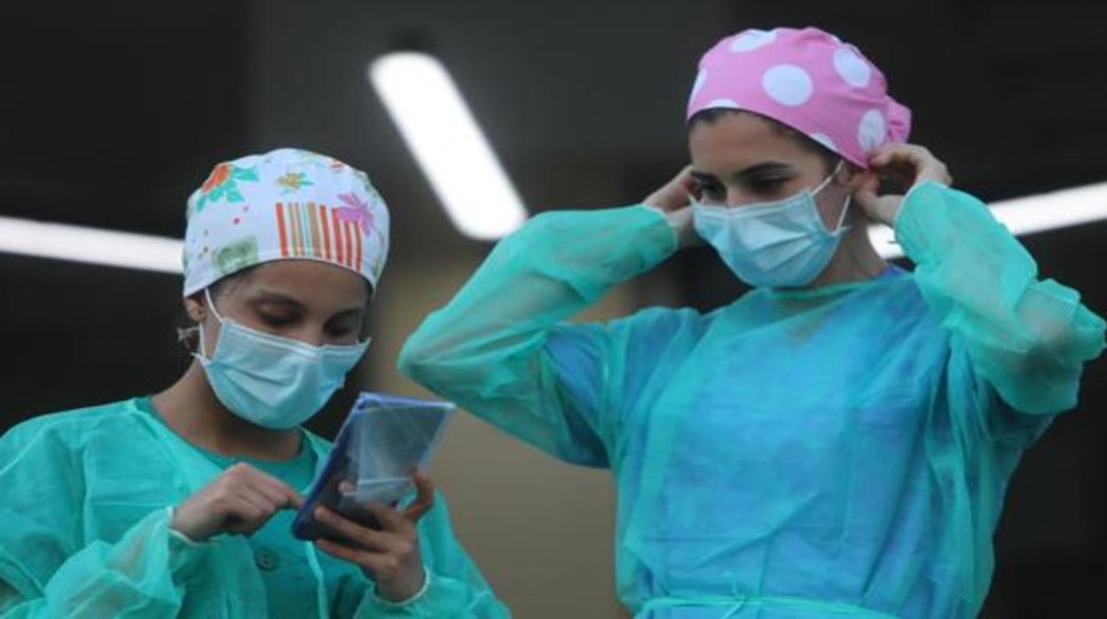 Dos sanitarias con gorros, mascarillas y batas.