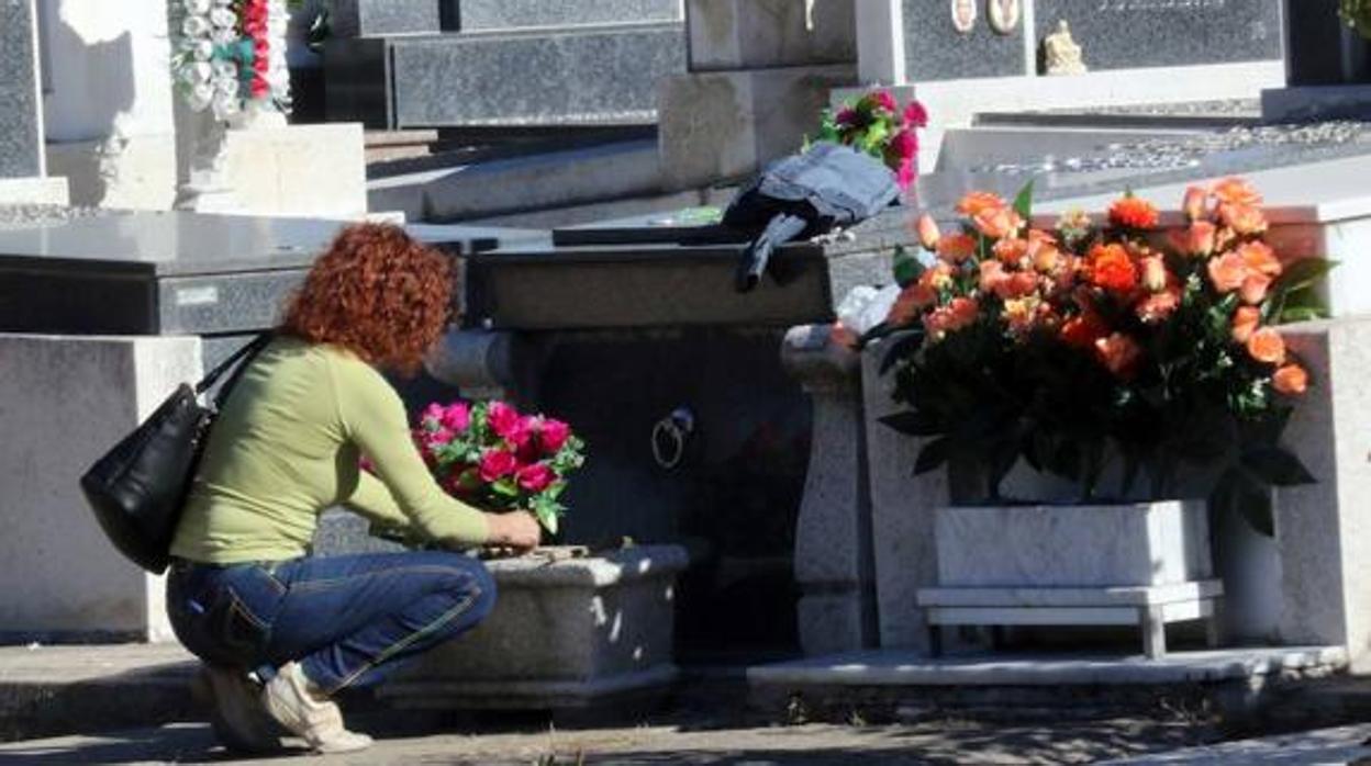 Una mujer deposita un ramo de flores en un cementerio