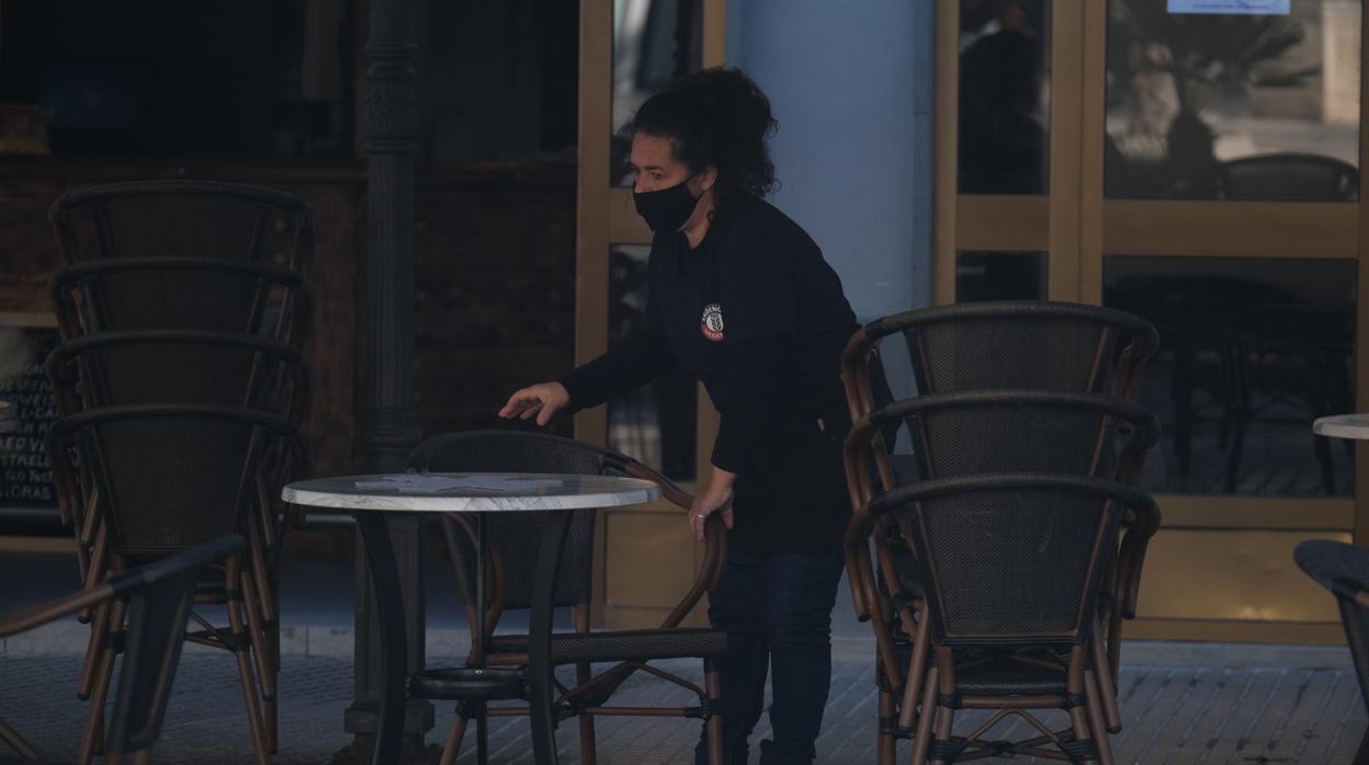 Una camarera recoge las sillas de una terraza en Cádiz capital.