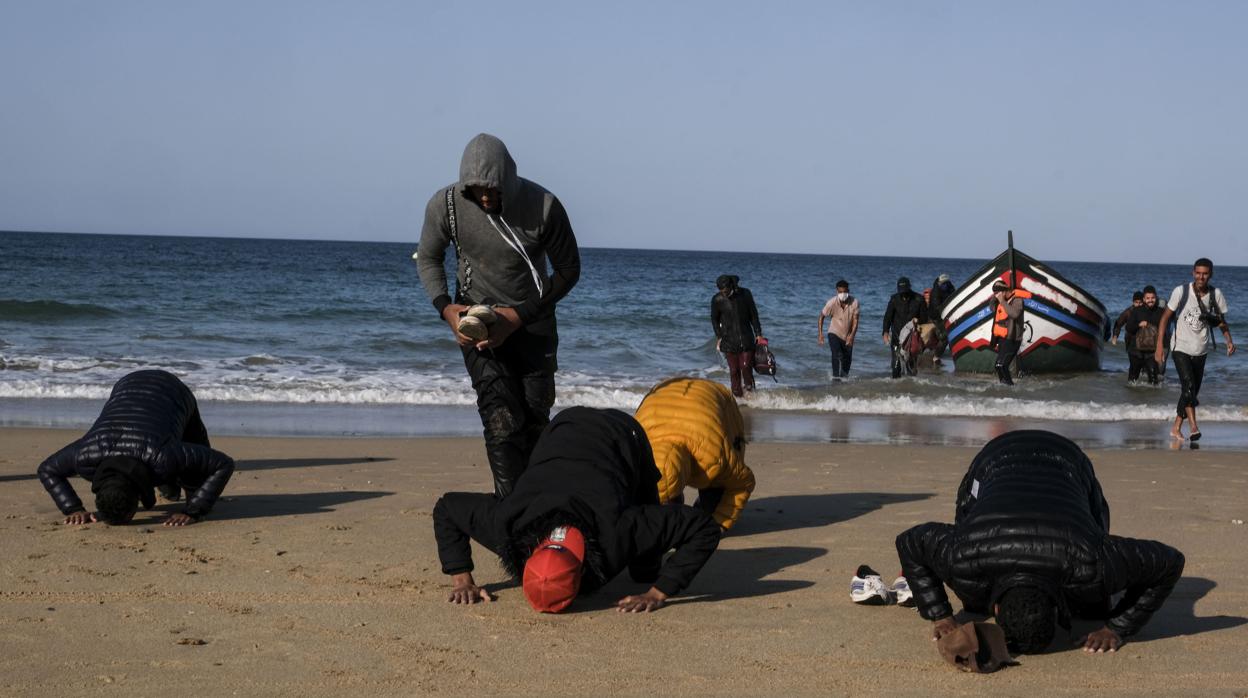 Unos inmigrantes rezan y besan la tierra en la playa Victoria.