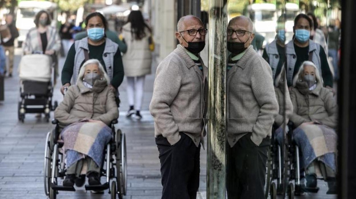 Varias personas por la calle se reflejan en el cristal de un escaparate