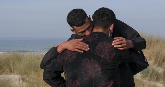 Dos migrantes se abrazan al llegar en patera a la playa de Cortadura en Cádiz.