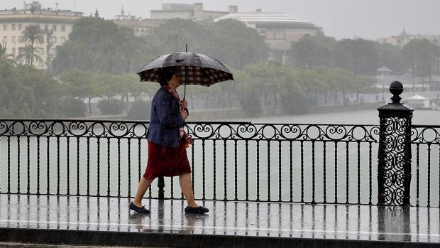 Una mujer se protege de la lluvia en el puente de Triana