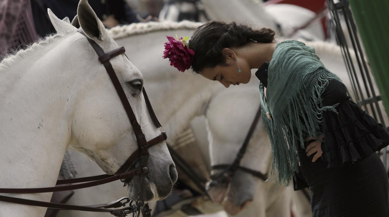 Una joven vestida de flamenca, junto al paseo de caballos