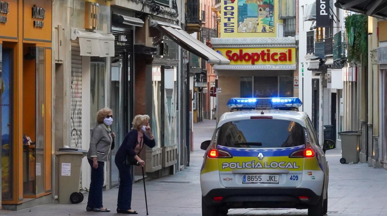 Un coche de la Policía Local se detiene ante dos personas que permanecen en una calle de Sevilla