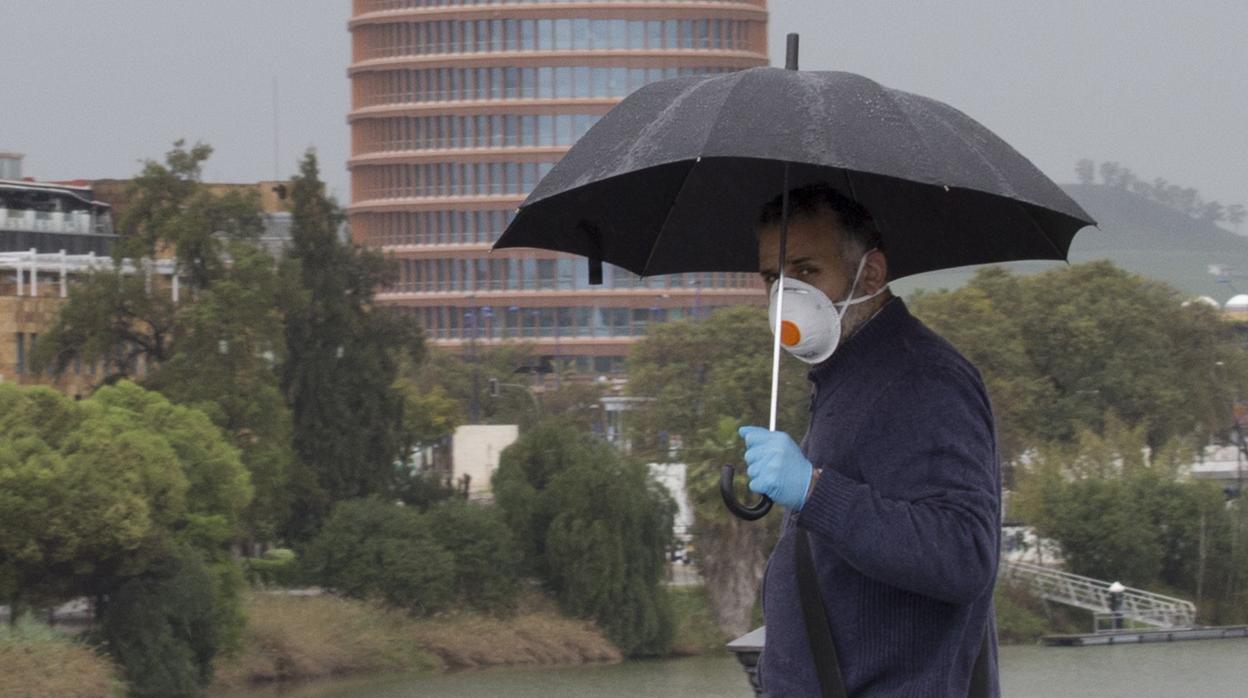 Un hombre pasea bajo la lluvia protegiéndose la cara con una mascarilla