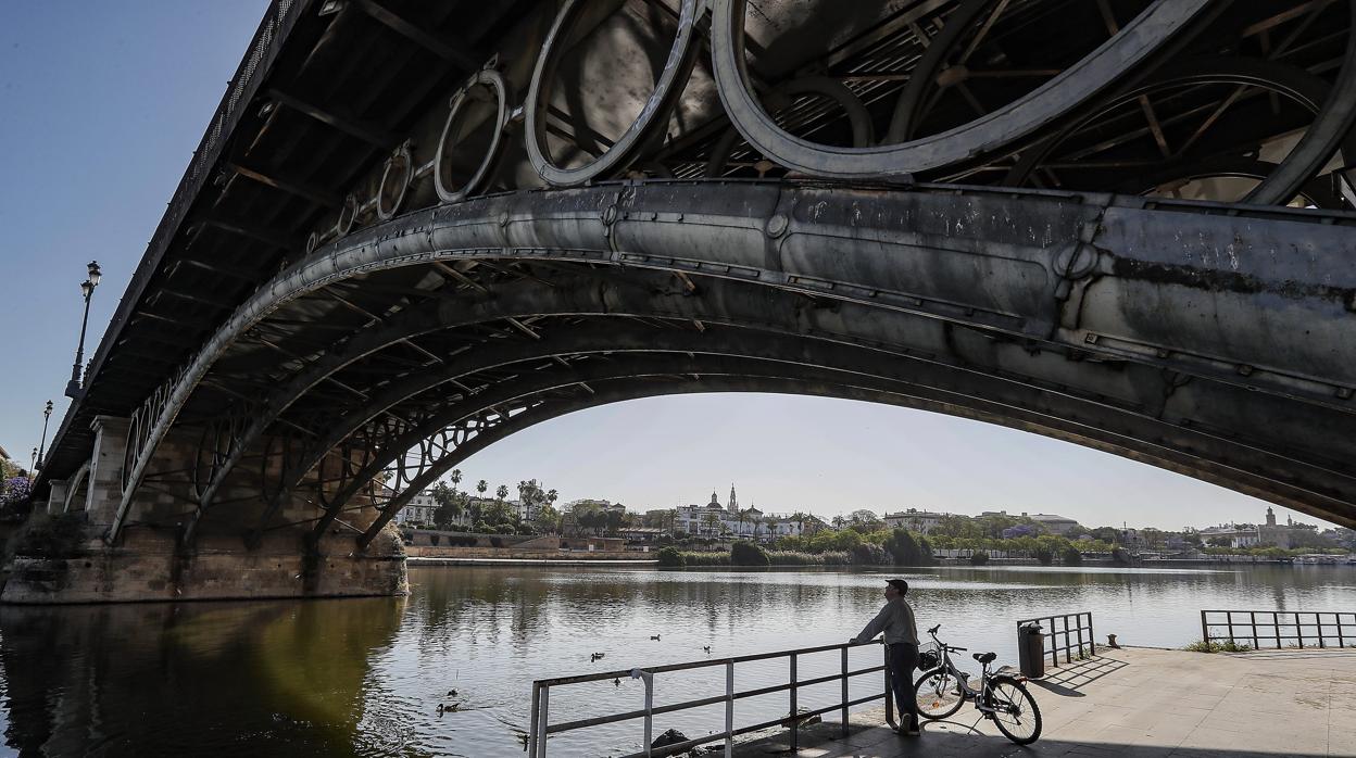 Un hombre visiona el río Guadalquivir bajo el puente de Triana