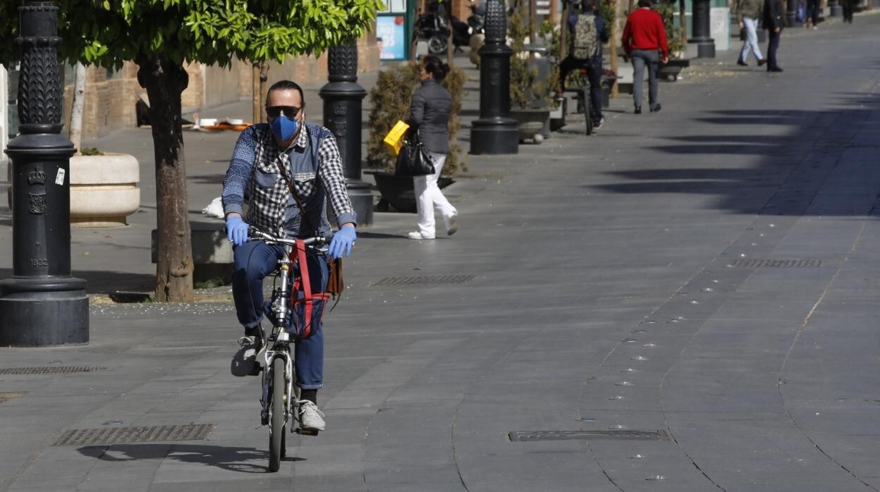 Un ciclista protegido con guantes y mascarilla por el centro de Sevilla