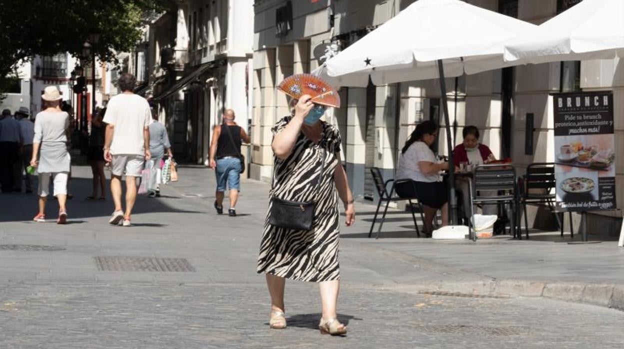 Una señora con mascarilla se protege del sol con un abanico en una calle de Sevilla