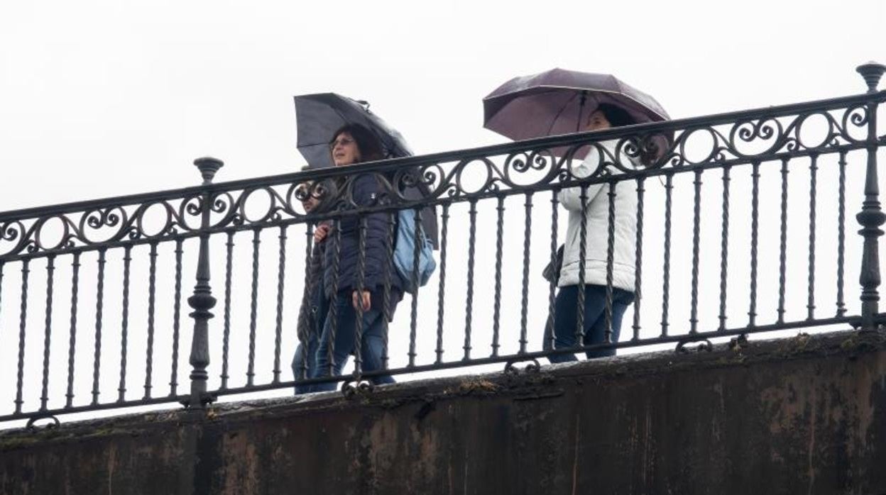 Un grupo de mujeres pasea por el puente de Triana con paraguas