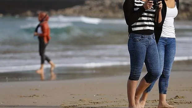Unas jóvenes pasean por la playa de la Zurriola de San Sebastián donde las temperaturas alcanzan estos días los 22 grados en las horas centrales