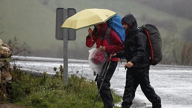Unos peregrinos caminan bajo la lluvia en Portomarin, Lugo, este lunes