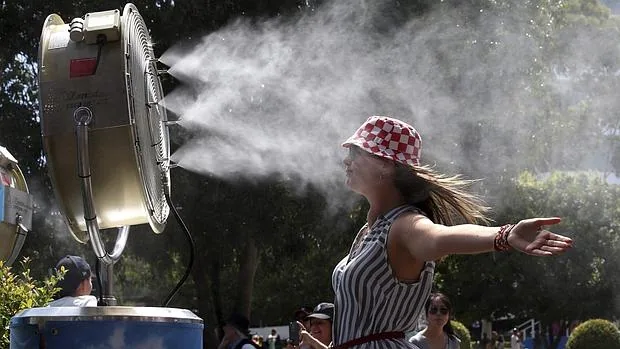Una joven sofoca el calor frente a un ventilador con nebulizador de agua en Australia