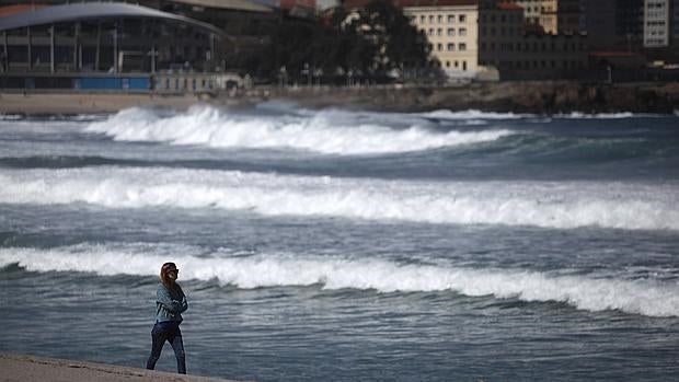 Una mujer pasea este lunes en la playa de Orzán, La Coruña, donde un frente dejará lluvias y viento