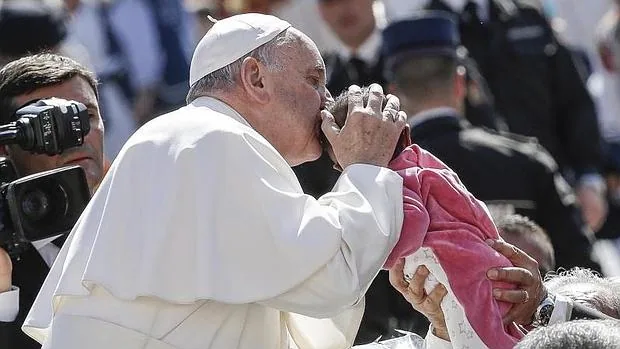 El Papa Francisco besa a un bebé a su llegada a la audiencia general de los miércoles en la plaza de San Pedro en el Vaticano