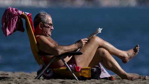 Un hombre lee el periódico en una playa de Málaga