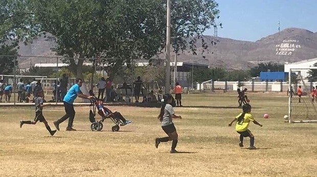 Un padre empuja la silla de ruedas de su hijo para que pueda jugar a fútbol