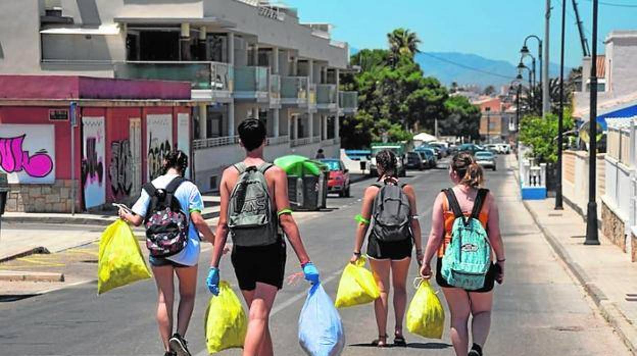 Cuatro jóvenes, con bolsas de basura, por una calle de Cabo de Palos