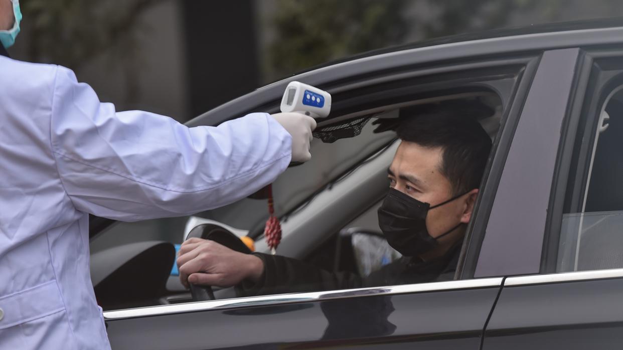 Un policía toma la temperatura a un conductor en un puesto de control, a la salida de Wuhan. Mongolia ha anunciado también hoy que cierra su frontera