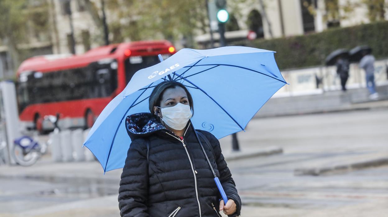 Una mujer con mascarilla y paraguas por las calles de Valencia