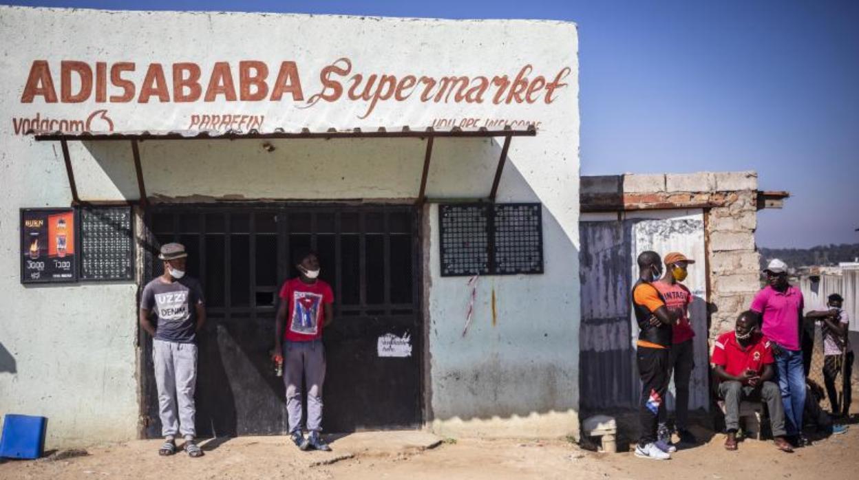 Un grupo de hombres con mascarillas esperan a que comience la entrega de alimentos a causa del coronavirus en Johannesburgo, Sudáfrica