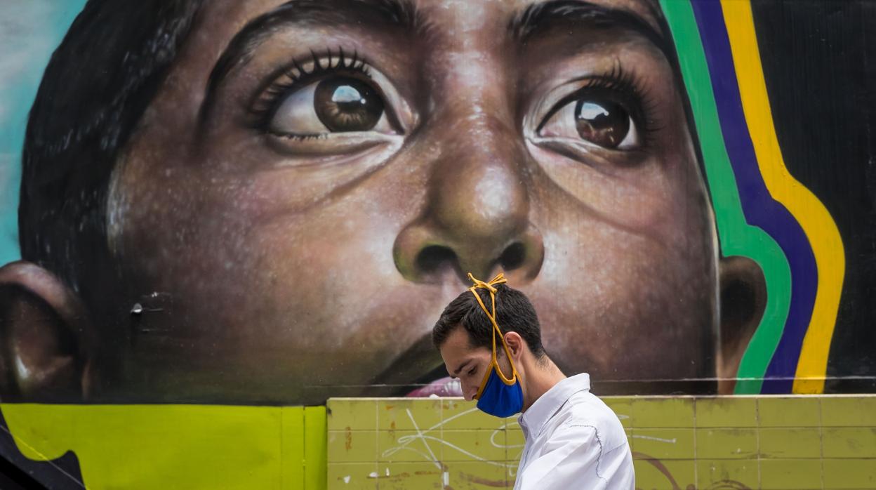 Un hombre con una mascarilla camina frente a un mural en Caracas