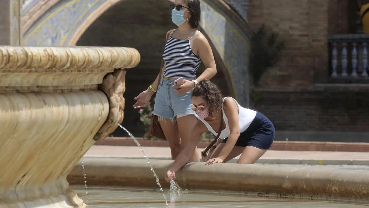 Dos jóvenes se refrescan en una fuente en Sevilla