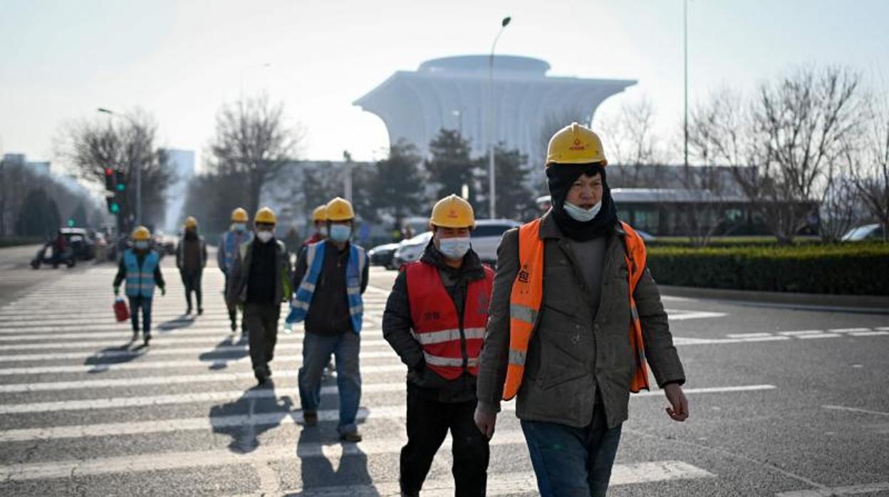 Un grupo de trabajadores con mascarilla cruzan este domingo una calle de Pekín