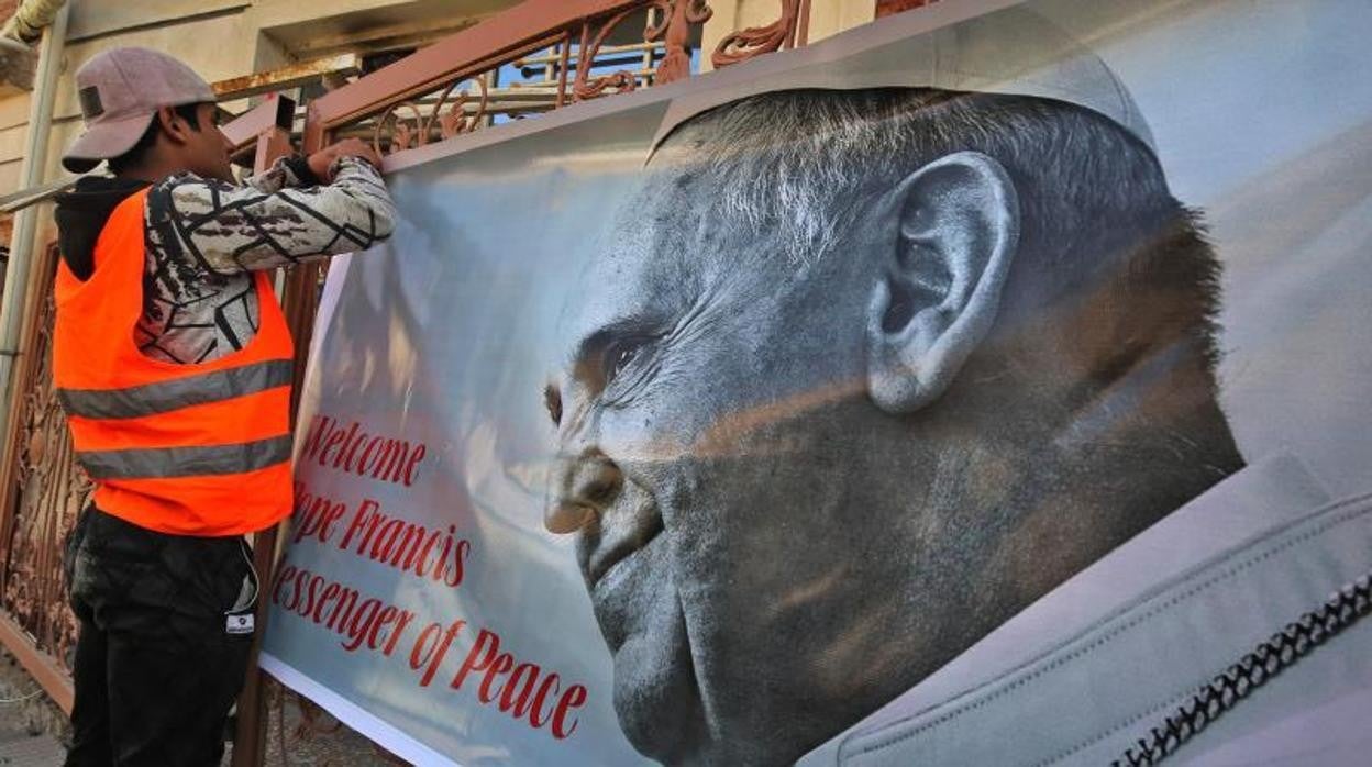 Un trabajador pasa junto un cartel de bienvenida al Papa en Qaraqosh, Iraq