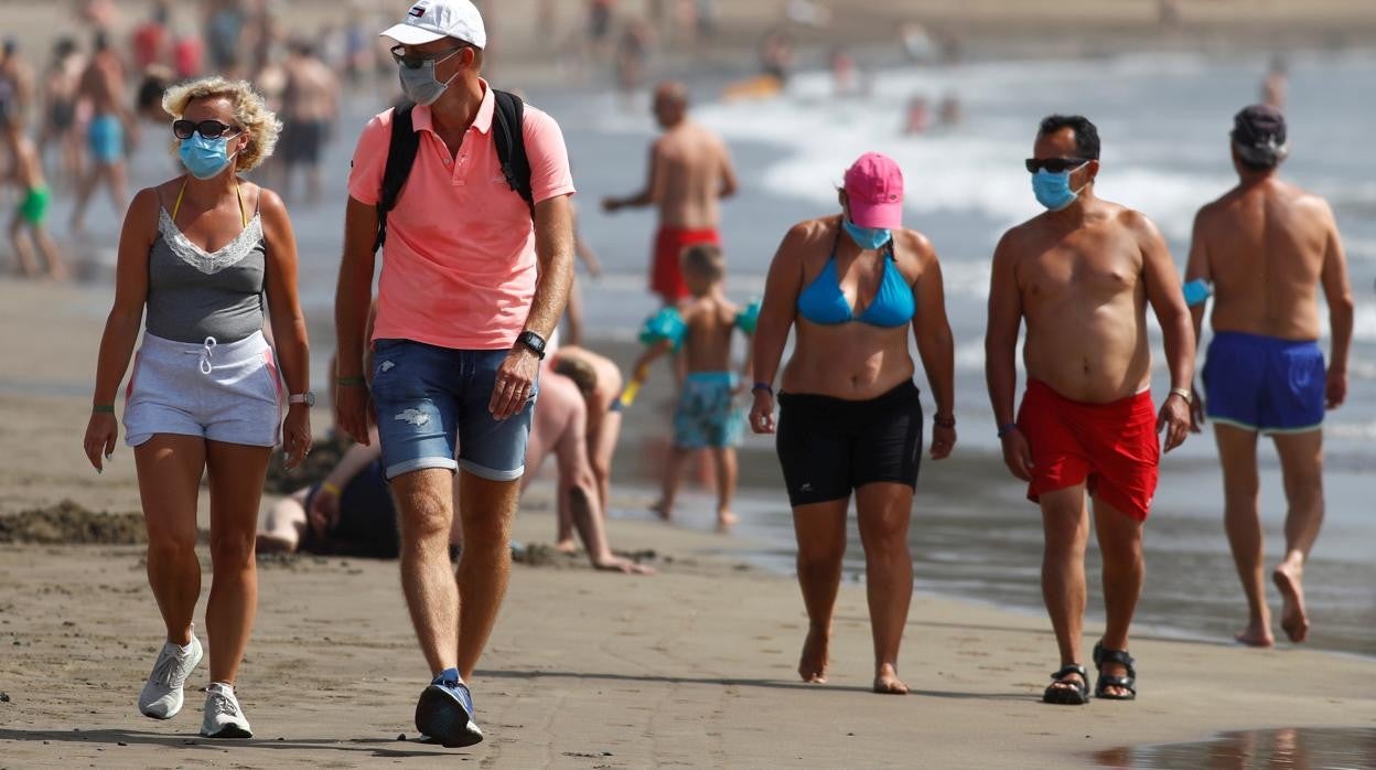 Turistas pasean con mascarilla por la Playa del Inglés, en Canarias