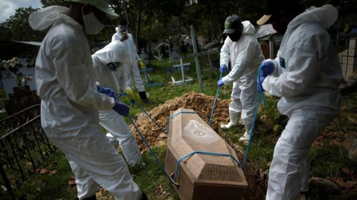 Trabajadores del cementerio Recanto da Paz entierran el ataúd de un hombre que murió por coronavirus